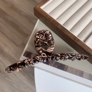 Detailed close-up of a large tortoiseshell acetate hair claw clip on a wooden box