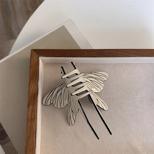 Detailed top view of a cream dragonfly hair claw with black wing patterns on a wooden tray