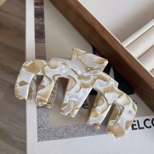 Gros plan d'une grande pince à cheveux en acétate avec texture marbrée crème et brillante