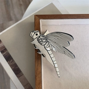 Detailed view of a cream dragonfly hair claw clip with black outlines on wood