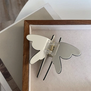 Top view detail of a dragonfly hair claw clip with cream finish and black edges on a tray