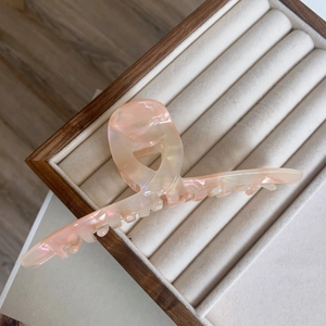 Macro detail of large acetate claw clip in pearlescent pink on wooden stand