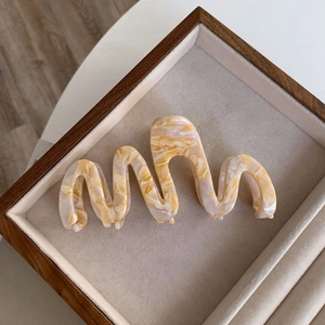 Detail of wavy acetate hair claw with cream and amber marble texture on display tray