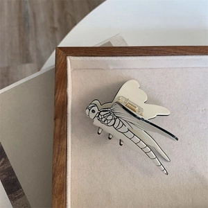Detail of dragonfly hair claw clip with black line textures on creamy white acetate base