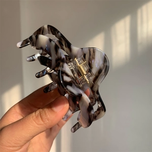 Detail of large acetate hair claw clip featuring elegant marble texture and gold metal spring