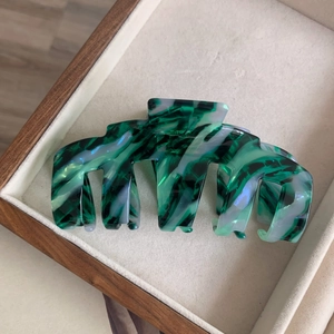 Grande pince à cheveux en acétate avec motif marbre vert présentée dans un plateau en bois