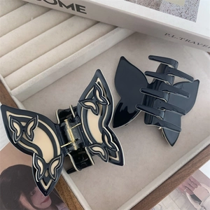 Detail view of two butterfly acetate hair claws in black and cream on a beige tray