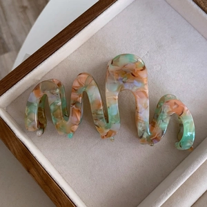 Detail view of wavy acetate hair claw clip with artistic marble texture on wooden tray
