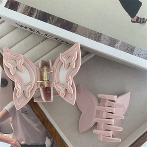 Close-up of pink butterfly hair claw clip with detailed resin relief on a magazine background