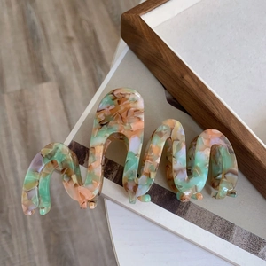 Close-up of oversized wavy acetate hair claw with green and orange marble texture