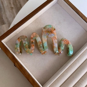 Detail of wavy acetate hair claw with pastel marble texture on beige jewelry tray