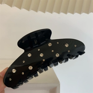 Gros plan d'une pince à cheveux noire brillante avec strass blancs sur blocs géométriques