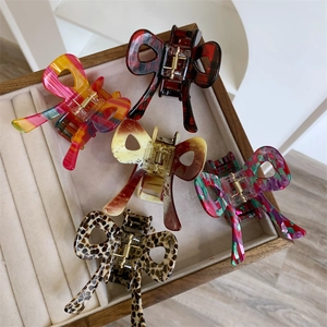Five assorted acetate bow hair claws in leopard, floral, and plaid patterns displayed in a box