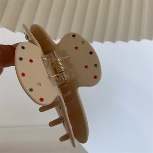Détail de la pince à cheveux en résine crème avec strass colorés et ressort doré brillant