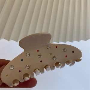 Détail d'une pince à cheveux crème ornée de strass colorés et de dents de préhension