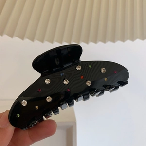 Détail d'une pince à cheveux noire avec strass colorés vue dans une main levée