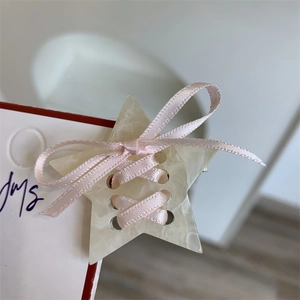 Détail d'une pince à cheveux étoile marbrée crème avec un petit nœud en ruban rose
