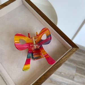 Colorful striped acetate bow hair claw clip with golden spring on velvet display tray