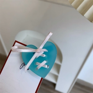 Vue macro détaillée de l'accessoire en acrylique en forme de cœur sarcelle avec nœud blanc