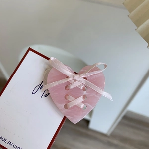 Détail d'une pince à cheveux cœur rose marbré avec nœud sur carte blanche