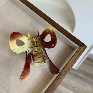 Detail of a medium acetate bow hair claw clip with tortoise pattern on a beige tray