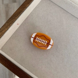 Detalle de pinza para el pelo naranja con forma de rugby y costuras blancas