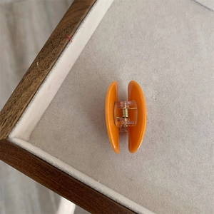 Primer plano de pinza para el cabello de acrílico naranja con resorte dorado en bandeja