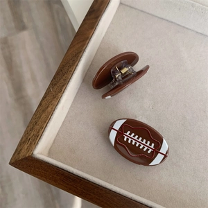 Detalle de dos pinzas para el cabello marrones con forma de fútbol americano en acetato