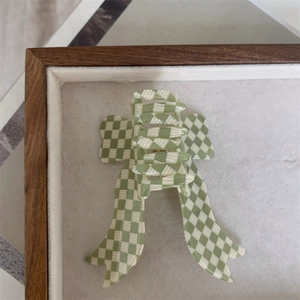 Detail view of a green and white checkered bow hair claw clip on a soft velvet jewelry tray