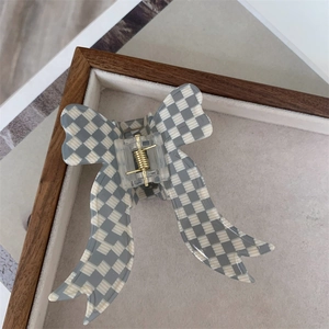 Close-up of a checkered bow hair claw clip with golden metal spring on a tray