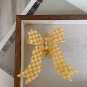 Detail view of large yellow and white checkered bow hair claw clip on velvet tray