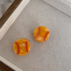Vista detallada de pendientes de béisbol amarillos con puntadas rojas sobre terciopelo
