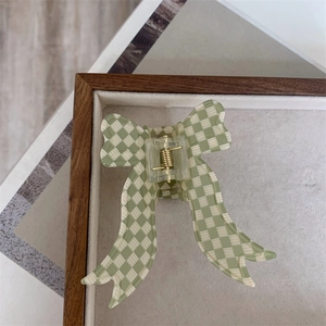 Detailed view of the bow-shaped hair claw with green and beige plaid pattern design