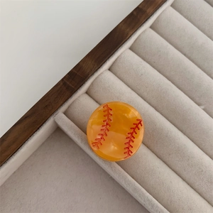 Detalle de una pinza para el pelo redonda amarilla de béisbol en bandeja de terciopelo blanco