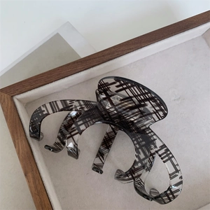 Detail of large translucent claw clip with black grid pattern on a beige display tray