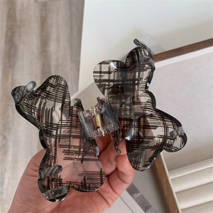 Detailed view of butterfly hair claw clip with black plaid pattern and gold metal spring