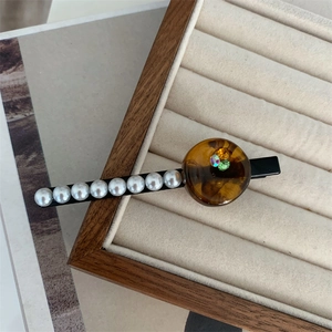 Close-up of pearl hair clip with amber resin and crystals on beige velvet tray