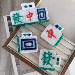 Mahjong-themed acetate hair claws set with red and green characters in a jewelry box
