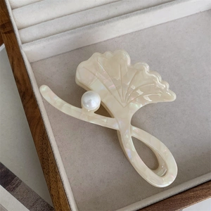 Detailed close-up of a pearlescent ginkgo leaf hair claw with an elegant white pearl