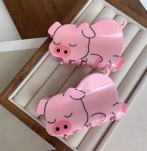Detail view of two cute pink pig hair claws made of glossy resin in a velvet jewelry box