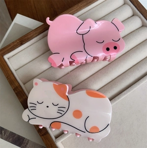Cute pink pig and spotted cat acrylic hair claws displayed on a beige velvet tray
