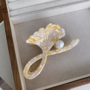 Detail view of acetate ginkgo leaf hair claw with white pearl on velvet jewelry box