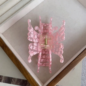 Détail d'une pince à cheveux papillon rose avec motif floral en acétate et ressort doré