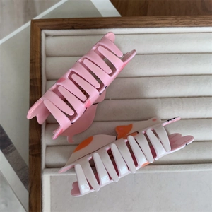 Detailed close-up of cute cat-shaped hair claws in pink and white on a velvet tray