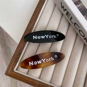 Détail de barrettes ovales noires et ambrées avec lettrage New York sur velours
