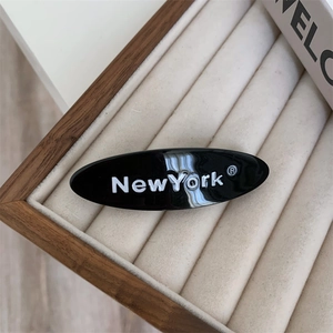 Détail d'une pince à cheveux ovale noire avec texte New York dans une boîte à bijoux
