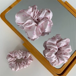 Detailed close-up of pink floral satin scrunchie with soft pleated texture on mirror