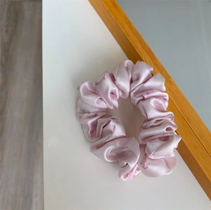 Close-up of pink floral satin scrunchie showing glossy fabric texture and pleats