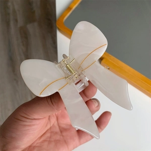 Detail of cream acetate bow hair claw clip with marble texture and gold accents