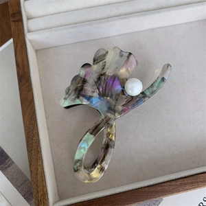 Detailed close-up of acetate ginkgo leaf hair claw with pearl accent on display tray